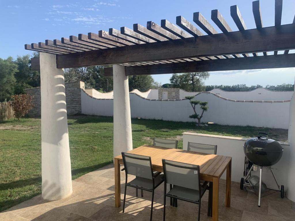 uma mesa de madeira e cadeiras sob uma pérgola em Appartement Domaine du soleil couchant em Saintes-Maries-de-la-Mer