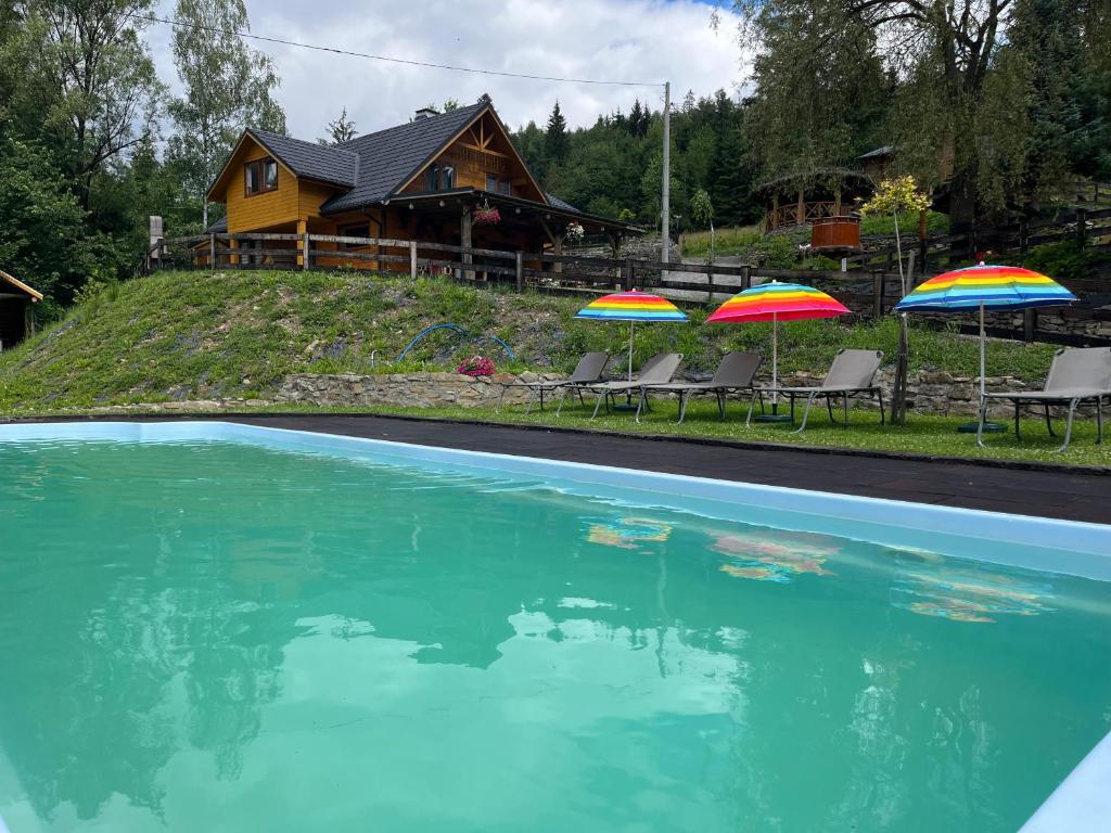 a swimming pool with two umbrellas and a house at Domek Kozia Grapka in Rajcza