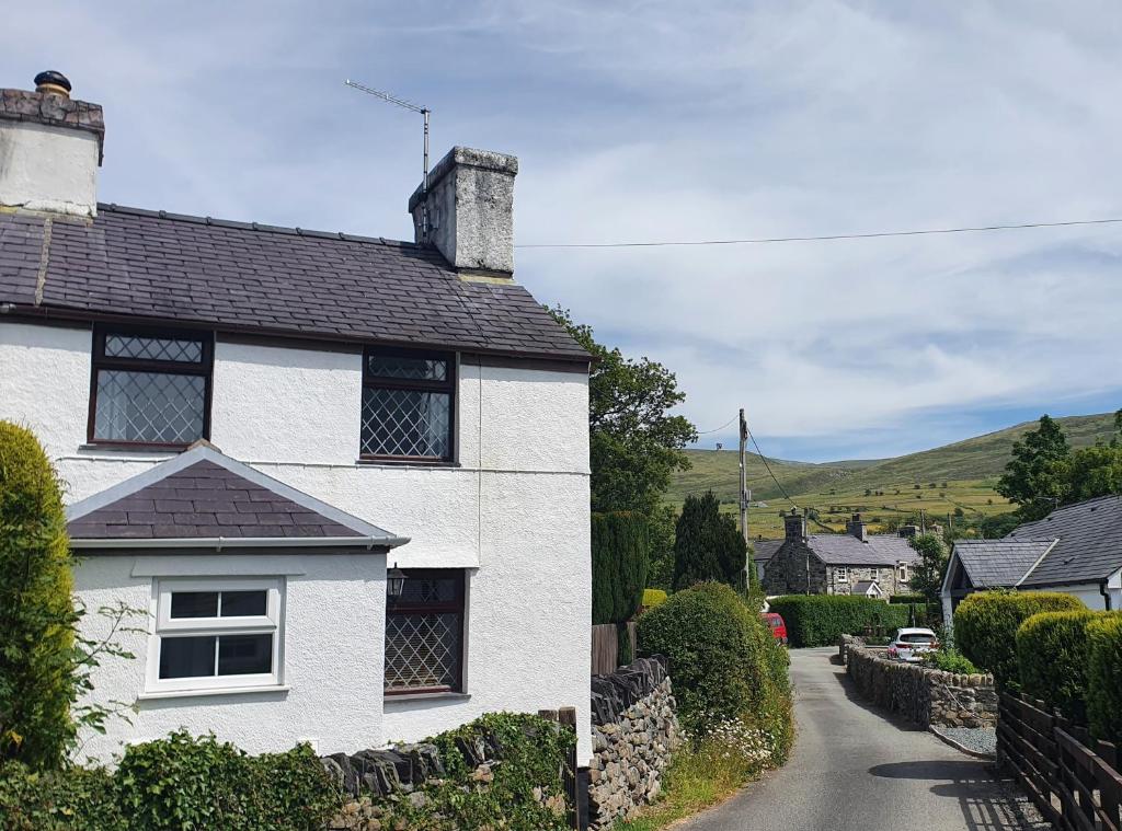 a white house with a black roof on a street at Green Cottage - Snowdonia in Llanllechid