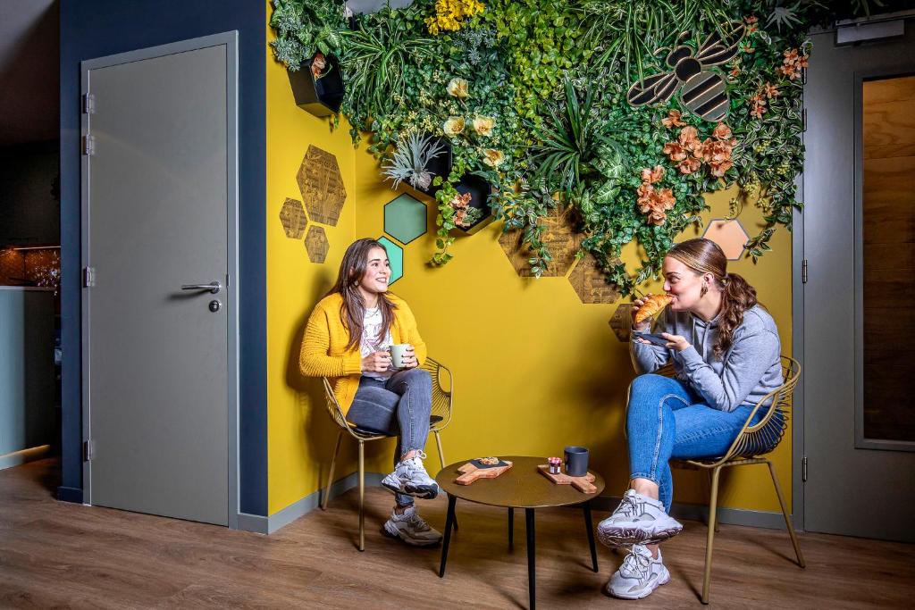 two women sitting in chairs in front of a yellow wall at The Bee Hostel in Amsterdam