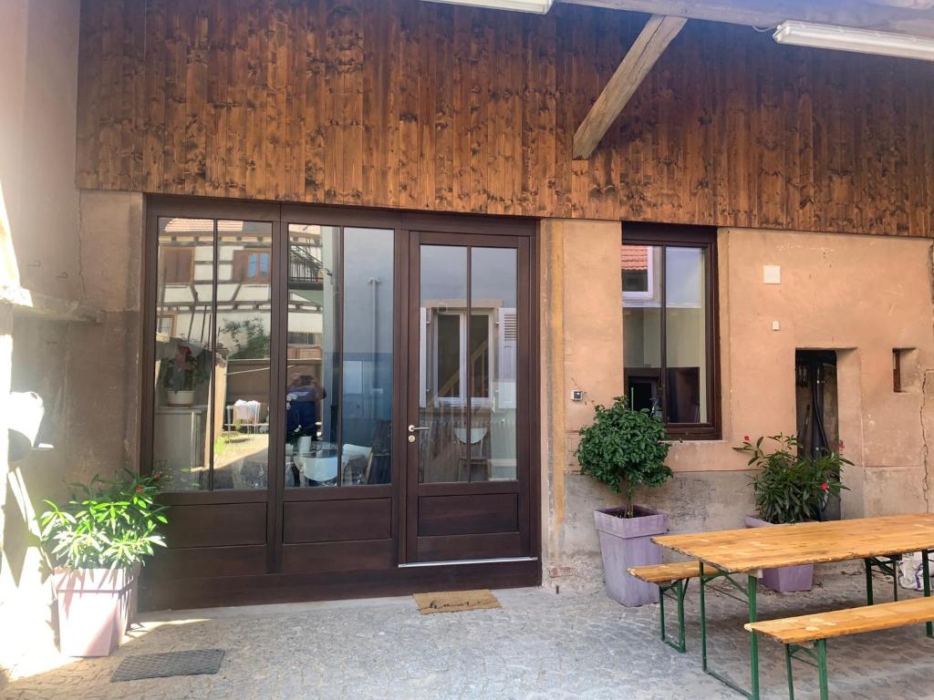 a building with a wooden door and a table and benches at la grange à Emile in Dambach-la-Ville