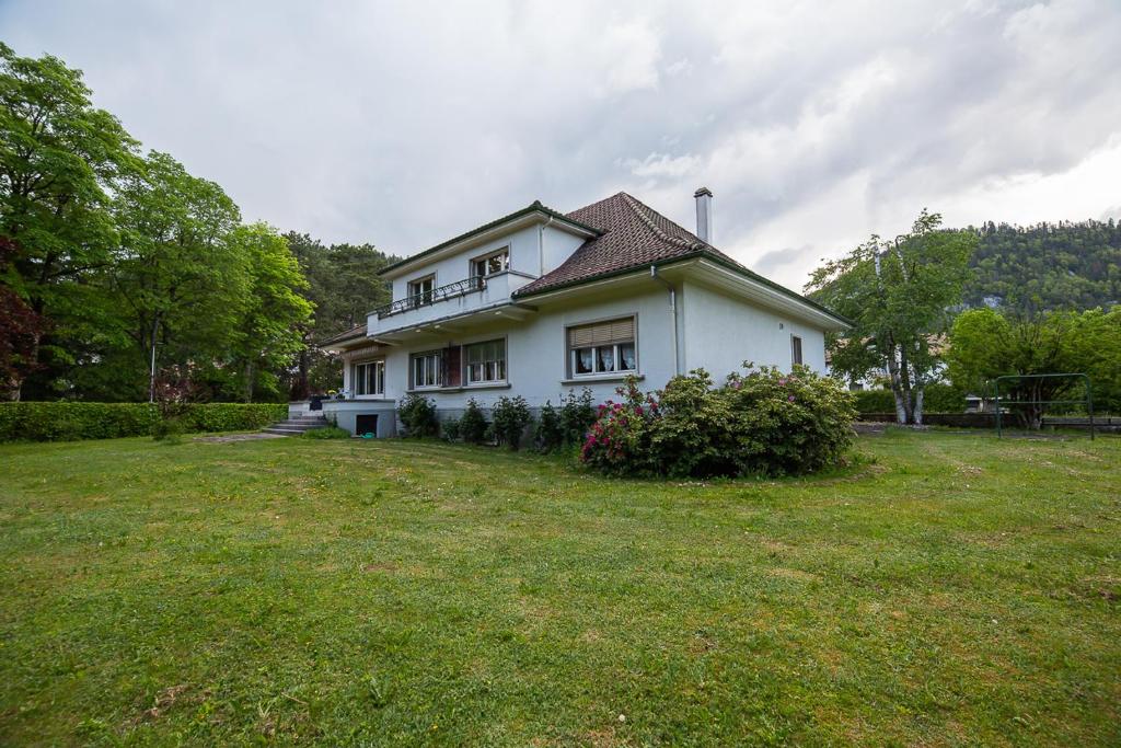 une grande maison blanche avec une cour en herbe dans l'établissement la viela, à Fleurier