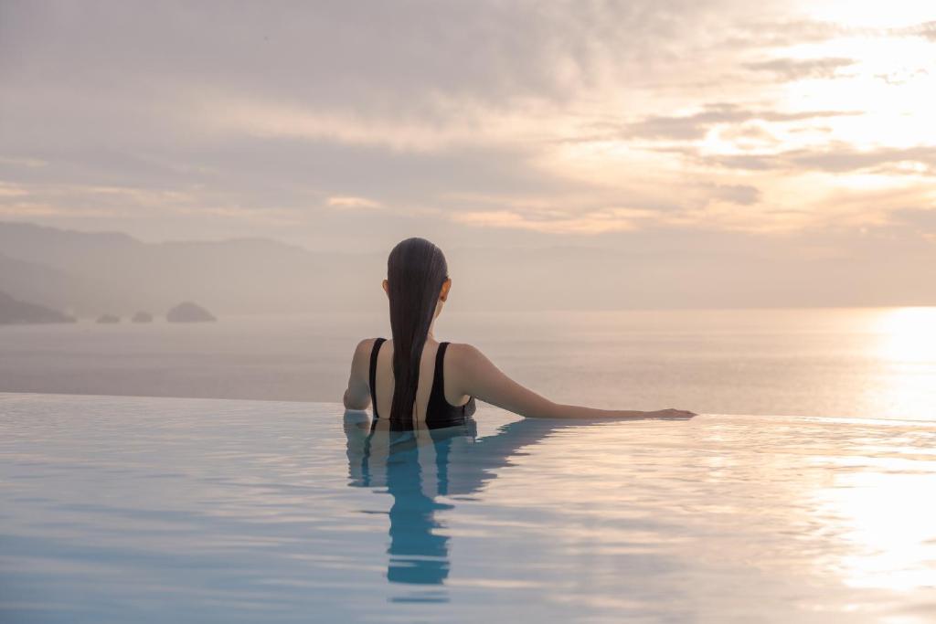 una mujer sentada en una piscina infinita viendo la puesta de sol en Maxwell Residences at Indah en Puerto Vallarta