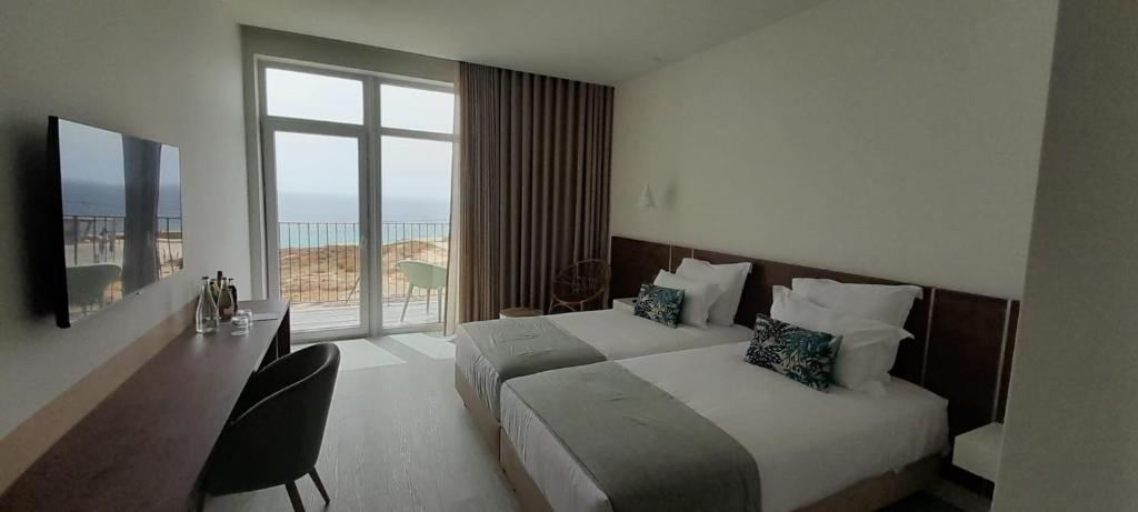 a hotel room with two beds and a large window at Porto Covo Praia Hotel & SPA in Porto Covo