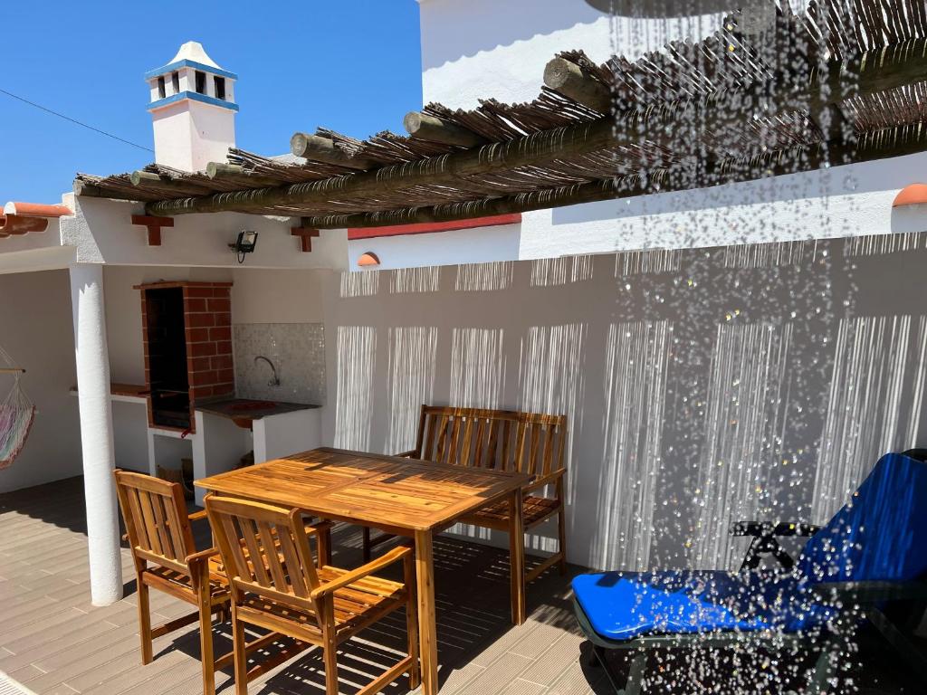 eine Terrasse mit einem Holztisch, Stühlen und einem Leuchtturm in der Unterkunft Casa das Dunas in Almograve