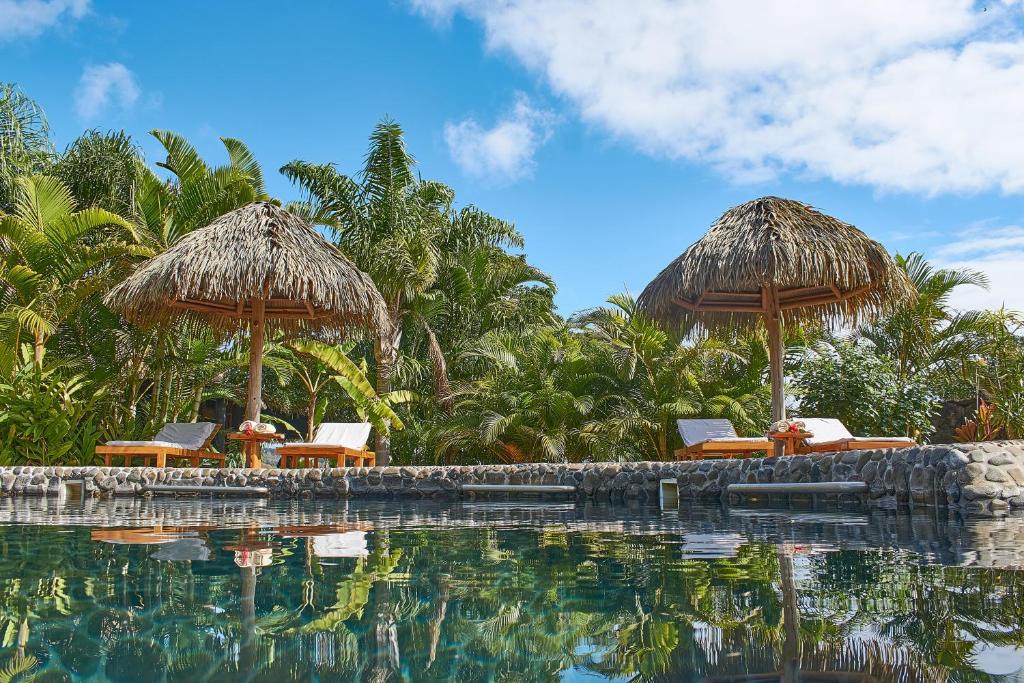 einen Pool mit Stühlen, Sonnenschirmen und Bäumen in der Unterkunft Hotel Hare Uta in Hanga Roa