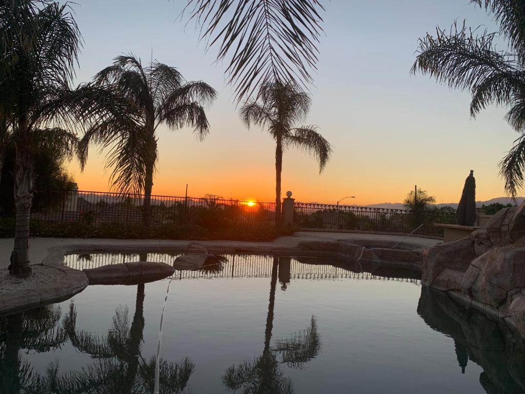 a sunset over a swimming pool with palm trees at LuxHome Suites & Villa in Riverside