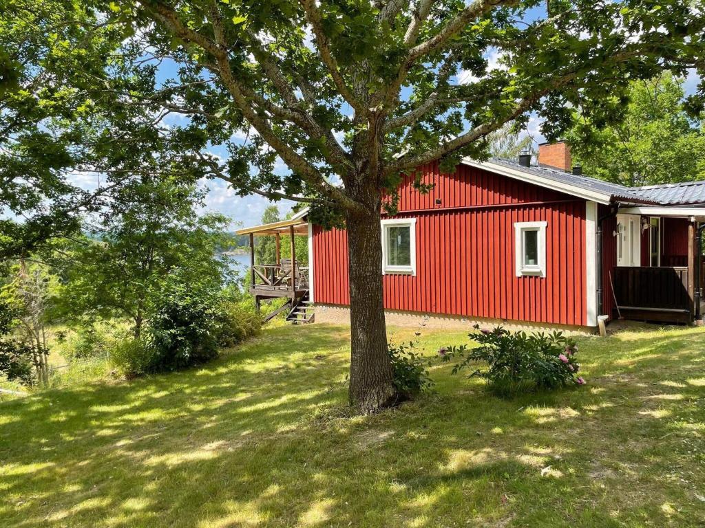 una casa roja con un árbol delante en Holiday home RIMFORSA V en Rimforsa