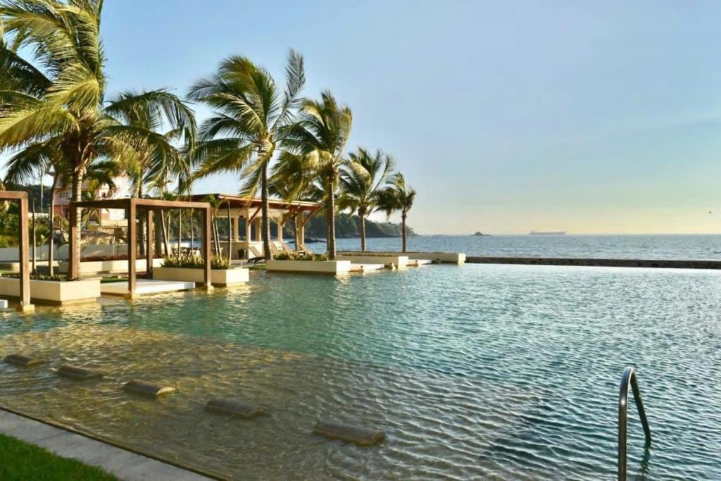 a swimming pool with palm trees and the ocean at Ponto Horizonte Manzanillo. Best place in Manzanillo!!! Luxury beach front condo, gorgeous views!! Best place you can stay!with up to 8 people. in Manzanillo