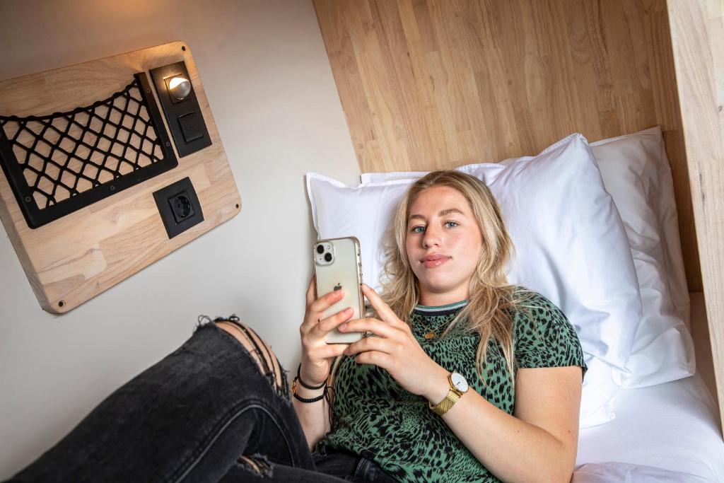 a woman sitting on a bed taking a picture with her cell phone at The Bee Hostel in Amsterdam
