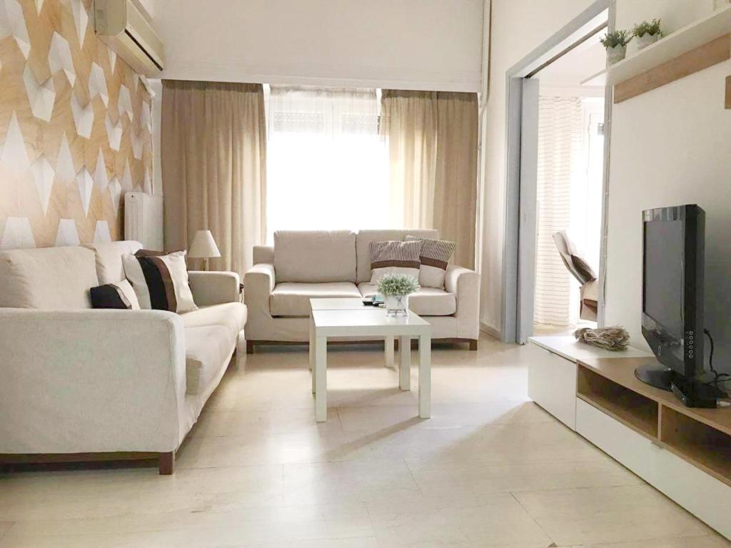 a living room with white couches and a tv at ΗΒΗ MINI HOME in Chalkida