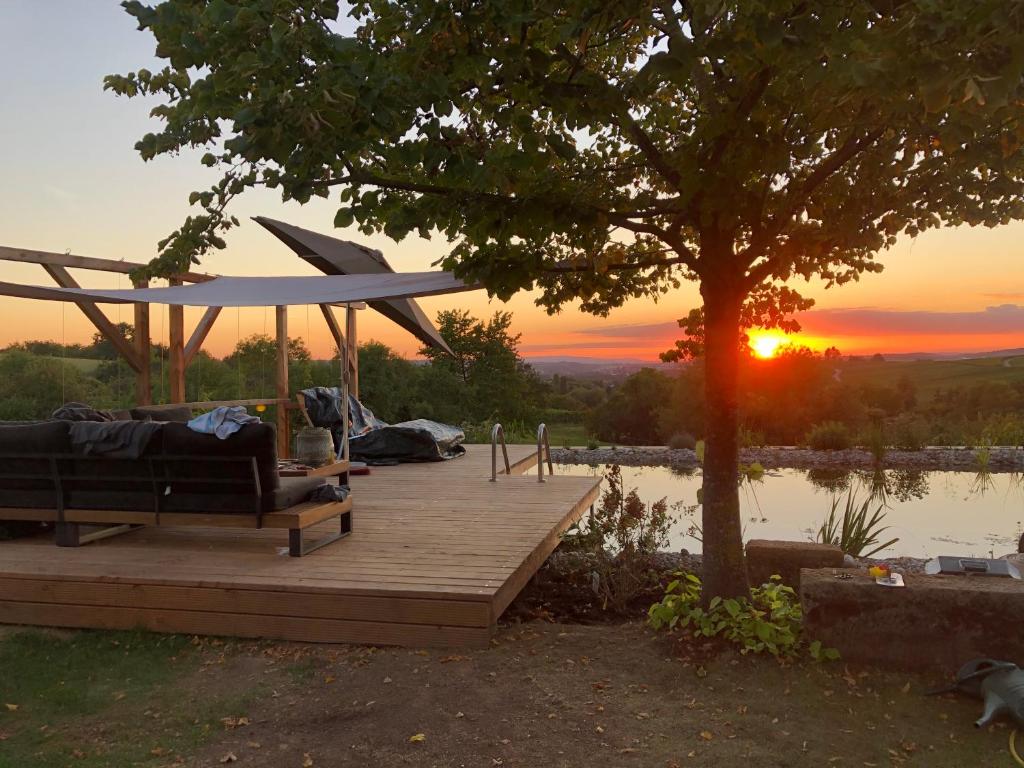 un banc sur une terrasse en bois avec un arbre et le coucher du soleil dans l'établissement 360 Grad - the view, à Ilsfeld