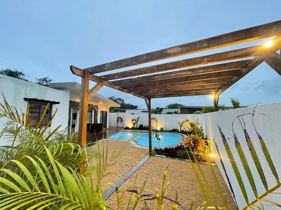 a backyard with a swimming pool and a wooden pergola at Villa des palmiers in Grand-Baie