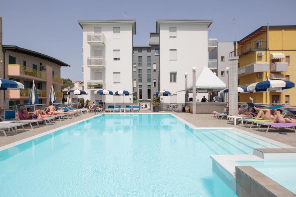 a large swimming pool with people sitting on chairs in a hotel at Hotel Bristol in Caorle