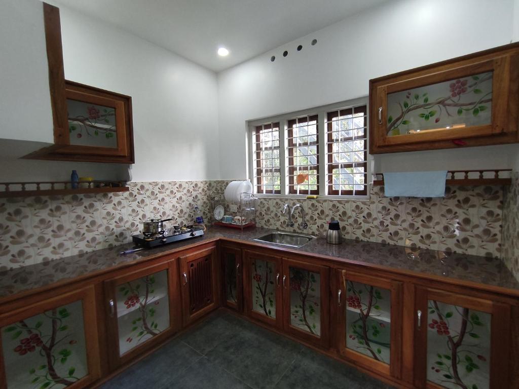 eine Küche mit Holzschränken, einem Waschbecken und Fenstern in der Unterkunft Moon Homestay in Santhanpara