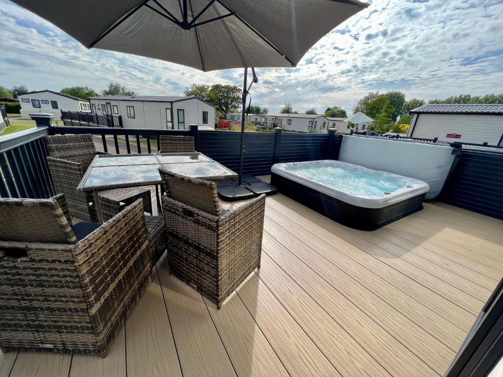 a deck with a hot tub and chairs and an umbrella at Honeysuckle Hot Tub Lodge in South Cerney