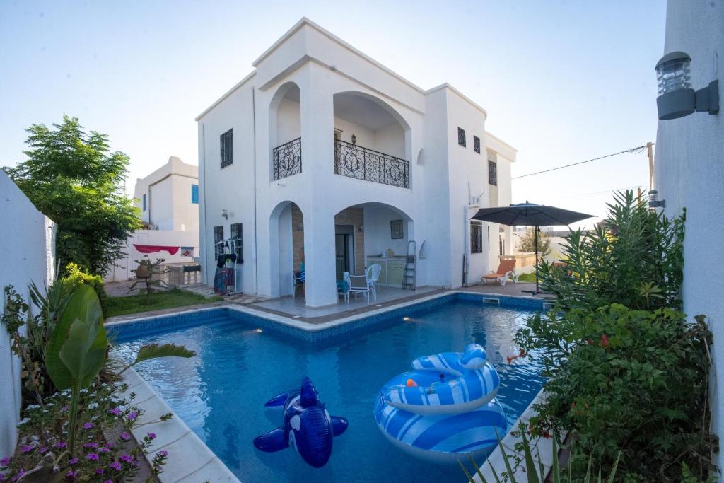 a swimming pool in front of a house with inflatables at Villa meublée avec piscine et abri de voiture in Erriadh