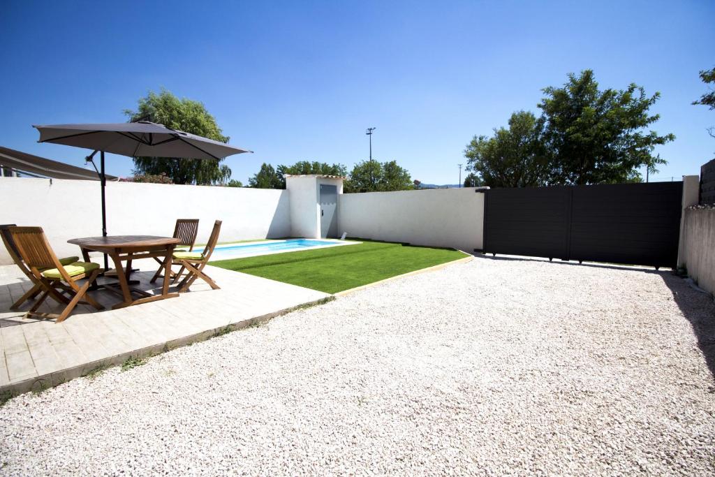 un patio con una mesa y una sombrilla junto a una valla en Jolie Maison avec piscine à 10min d’Aix enProvence, en Meyreuil