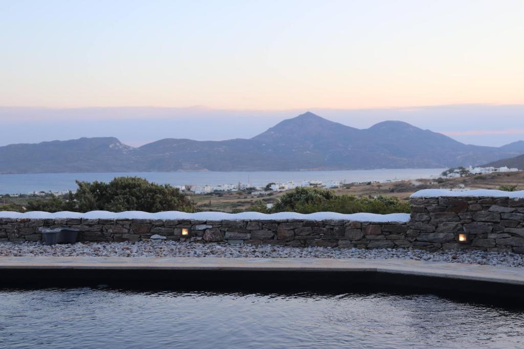 a swimming pool with a stone wall and mountains in the background at Valeria's House in Adamas