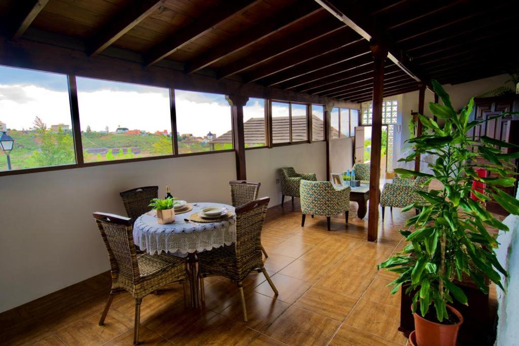 uma sala de jantar com mesa, cadeiras e janelas em Casa Cueva La Herencia em San Miguel de Abona