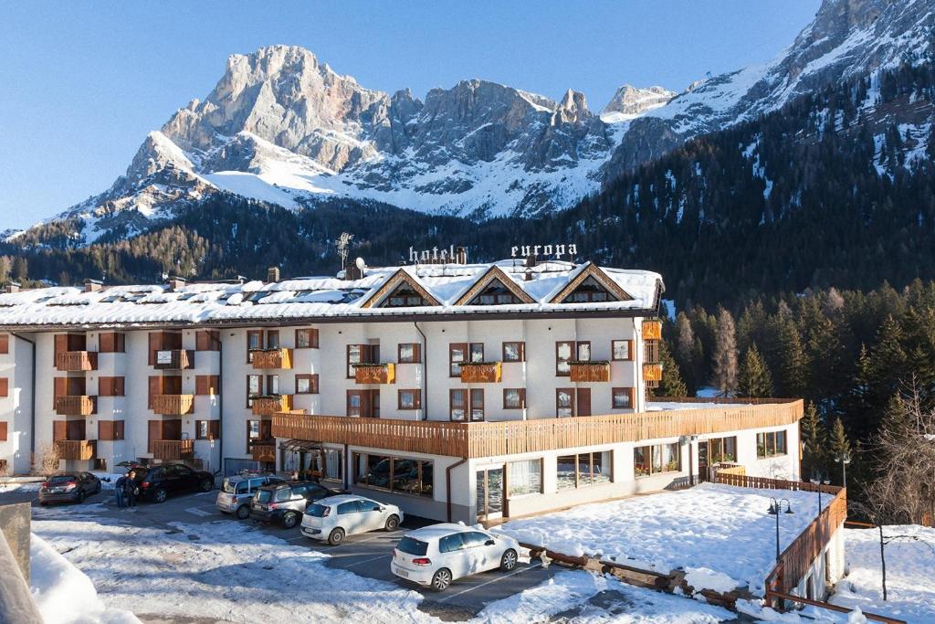 a hotel with cars parked in a parking lot in front of a mountain at Hotel Europa in San Martino di Castrozza