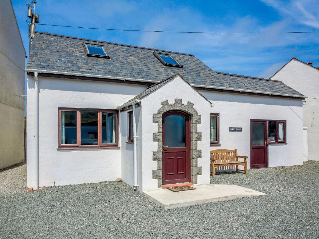 een wit huis met een rode deur en een bank bij Pen Y Bont in Aberdaron