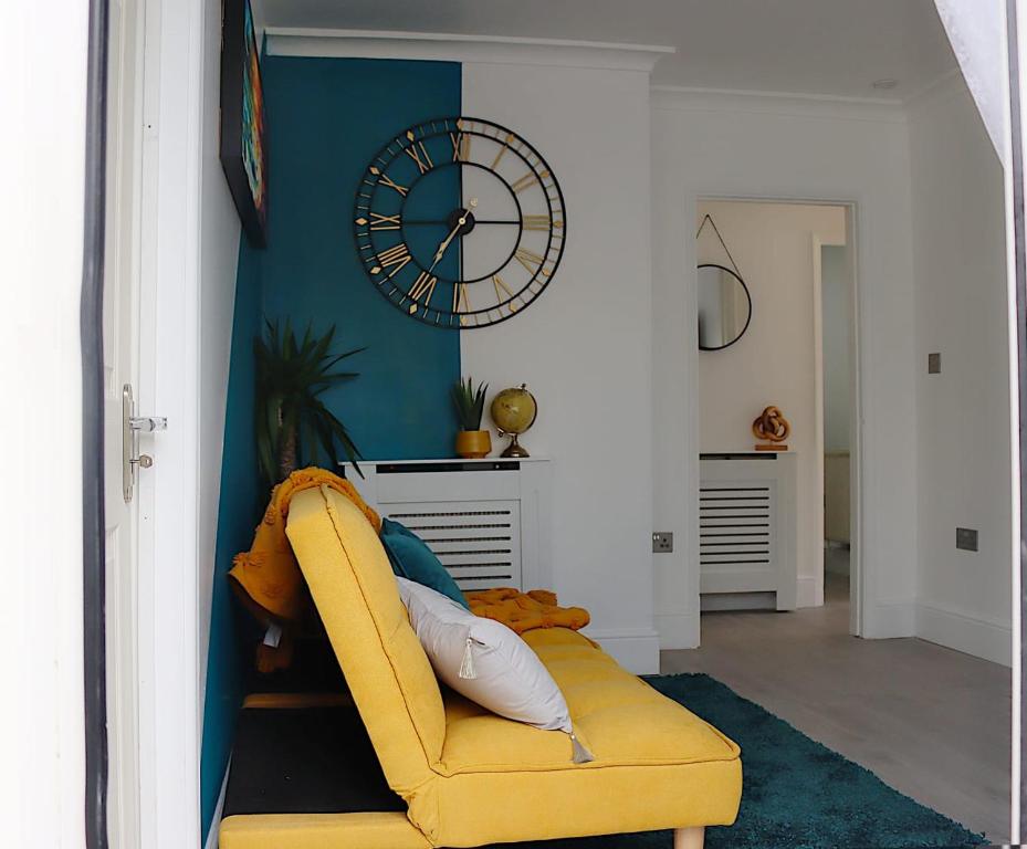 a yellow chair in a living room with a clock on the wall at Stunning 3 bedroom with patio and back garden in Bexleyheath