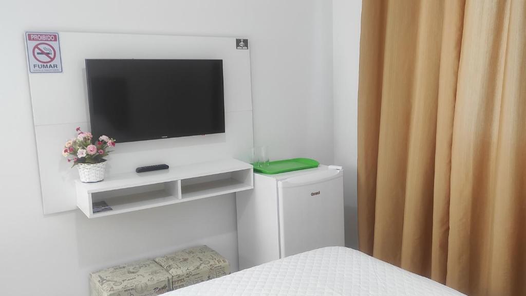 um quarto com uma televisão numa parede branca com uma cama em Mar dos Sonhos Suítes em Ubatuba