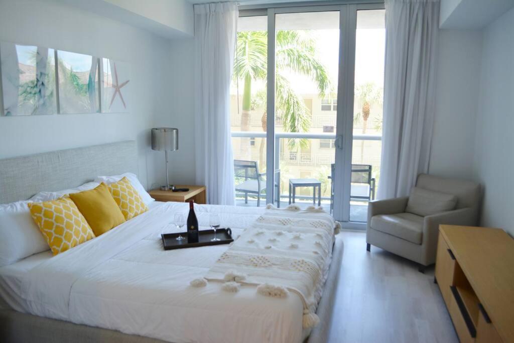 um quarto com uma grande cama branca e uma cadeira em Lovely 1 Bedroom condo 1 Bath w patio & kitchen em Hallandale Beach