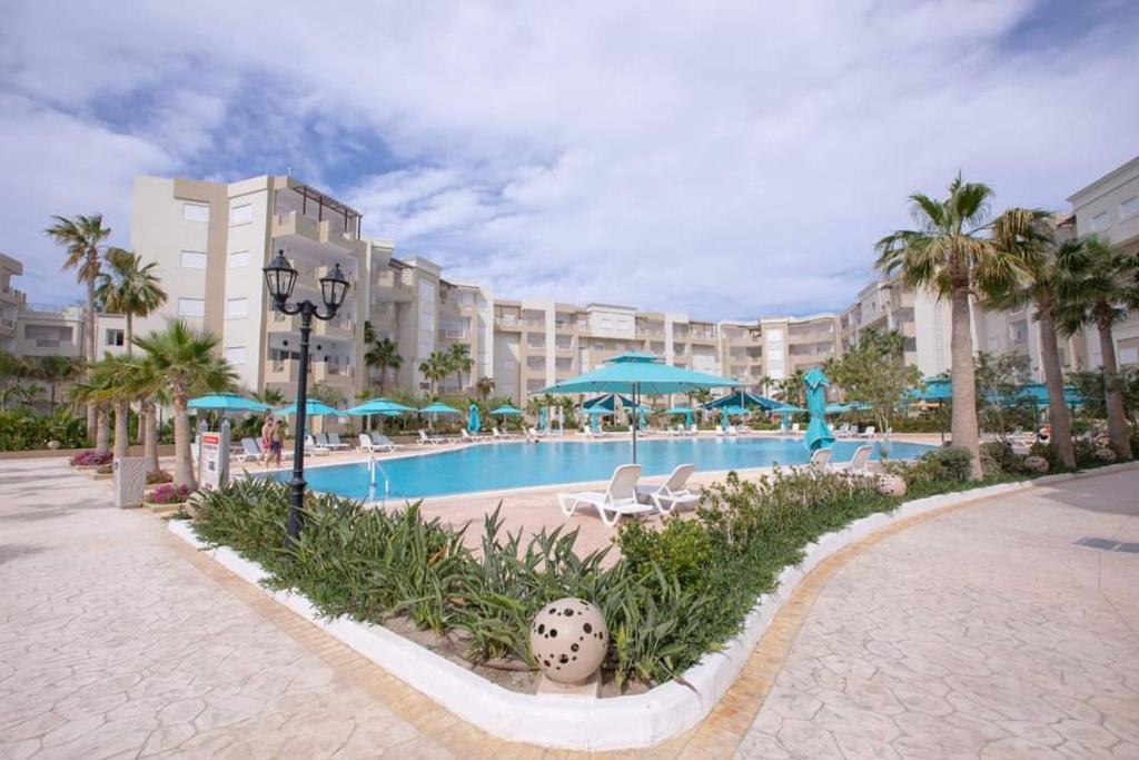 una piscina del resort con sedie, ombrelloni e palme di Splendide appartement au PALM LAKE RESORT a Monastir