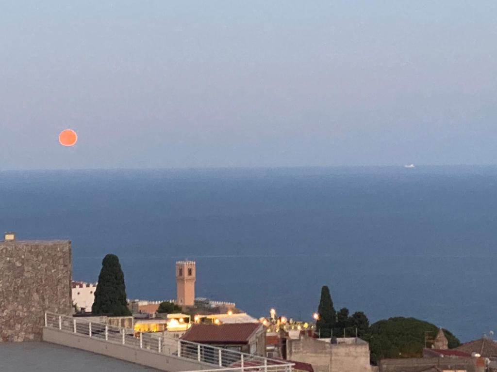 an orange moon rising over the ocean with a city at Murmuria Taormina in Taormina