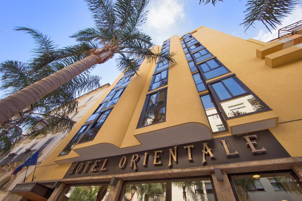 un bâtiment avec un panneau d'opérateur d'hôtel et un palmier dans l'établissement Hotel Orientale, à Brindisi