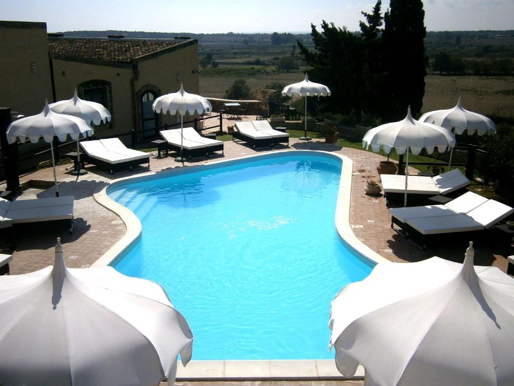 a swimming pool with white umbrellas and chairs at Hotel La Corte Del Sole in Noto