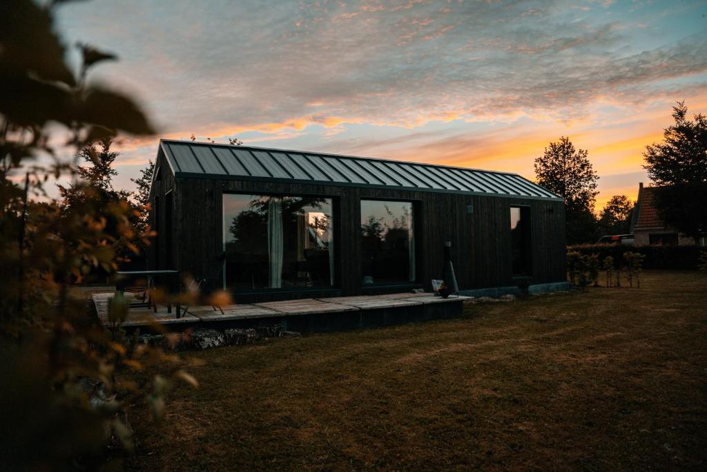 een klein zwart huis met een zonsondergang op de achtergrond bij Tiny house XXL in Bant