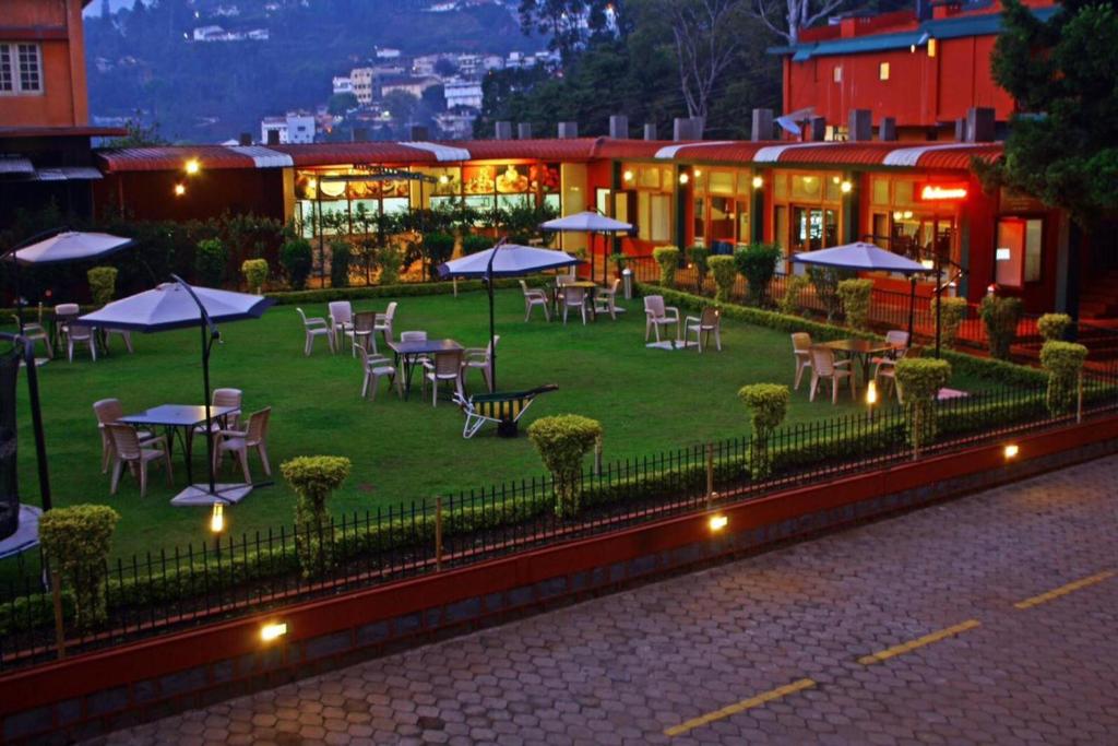 a restaurant with tables and chairs and umbrellas on a lawn at The HighGarden in Coonoor