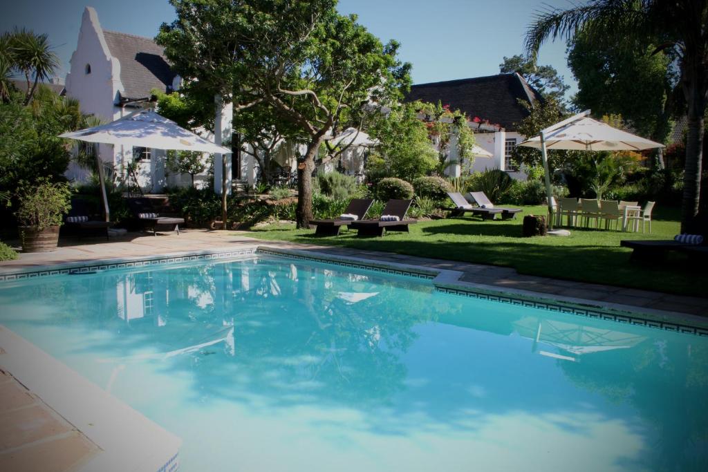 a swimming pool in a yard with chairs and umbrellas at Albourne Guesthouse in Somerset West