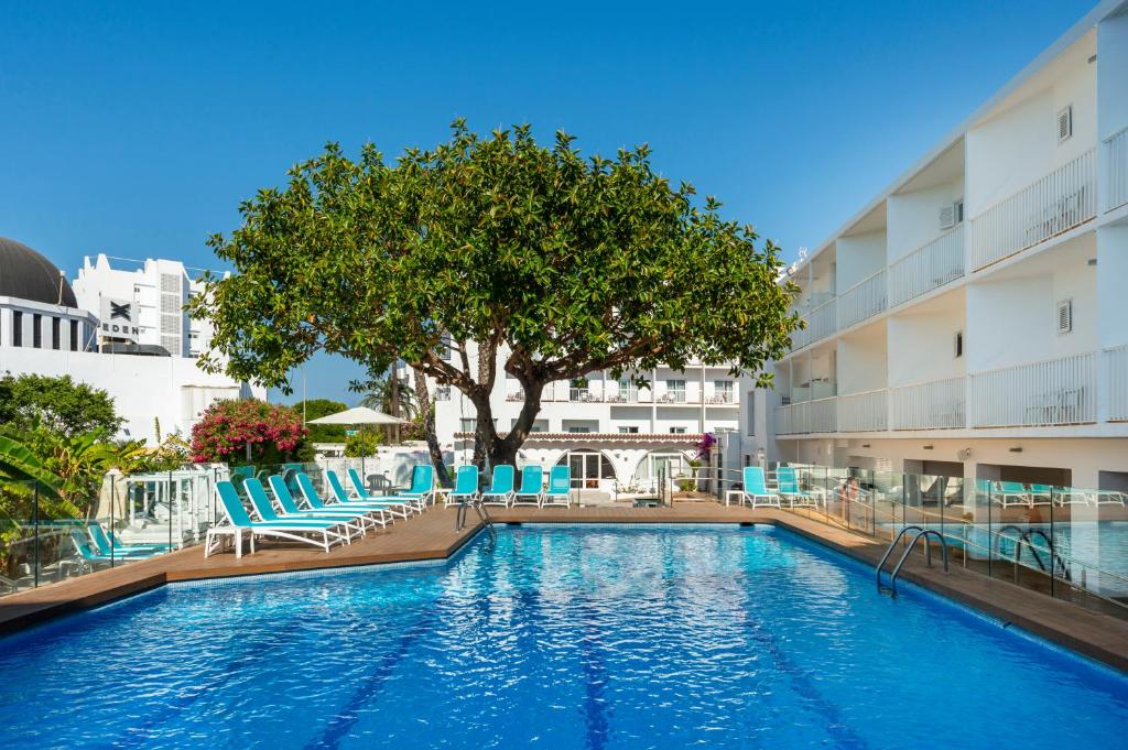 einem Pool mit Stühlen und einem Baum vor einem Gebäude in der Unterkunft Hotel Vibra Marco Polo II - Adults only in Sant Antoni de Portmany