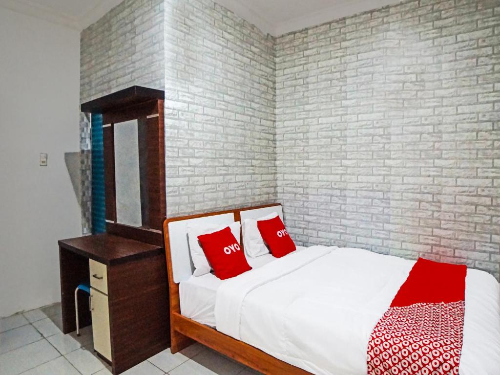 a bedroom with a bed with red pillows and a brick wall at OYO 91418 Kantil Homestay Syariah in Sunggal