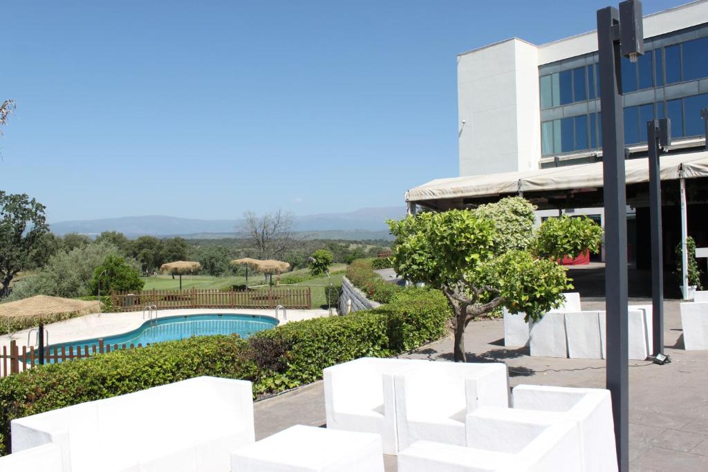 uma vista para um edifício com cadeiras brancas e uma piscina em Hospedium Hotel Valles de Gredos Golf em Talayuela