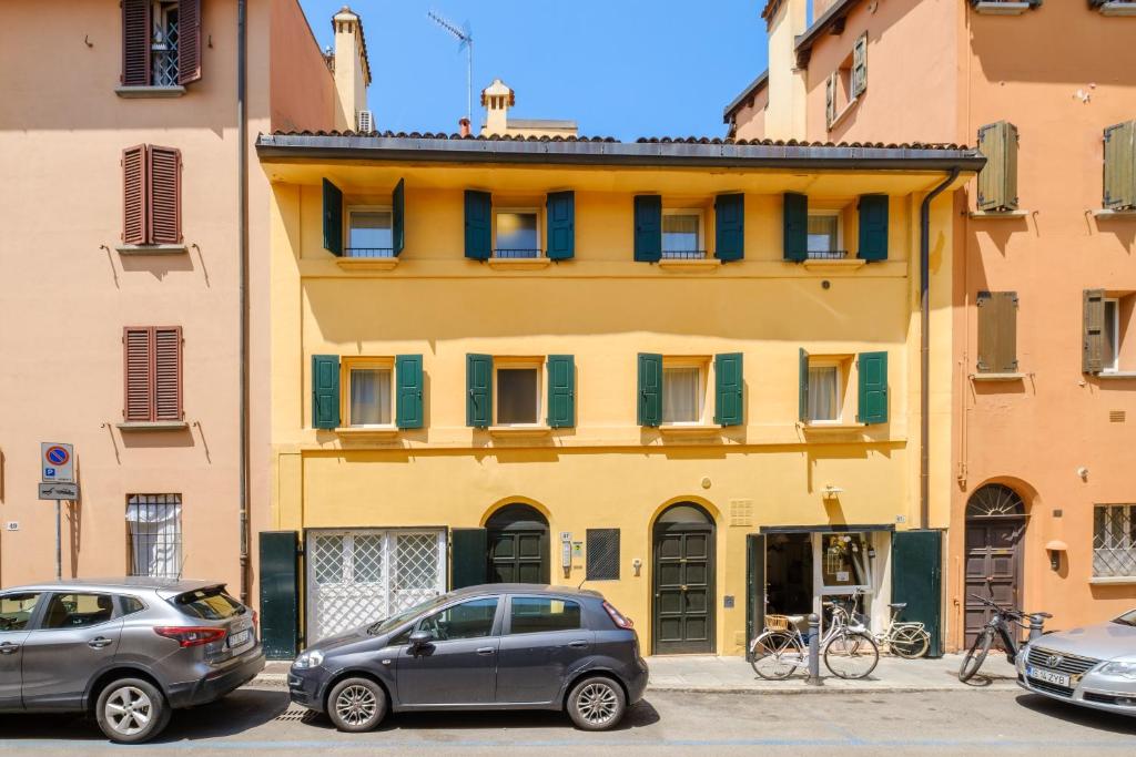 due auto parcheggiate di fronte a un edificio giallo di Frassinago Suites-BolognaRooms a Bologna
