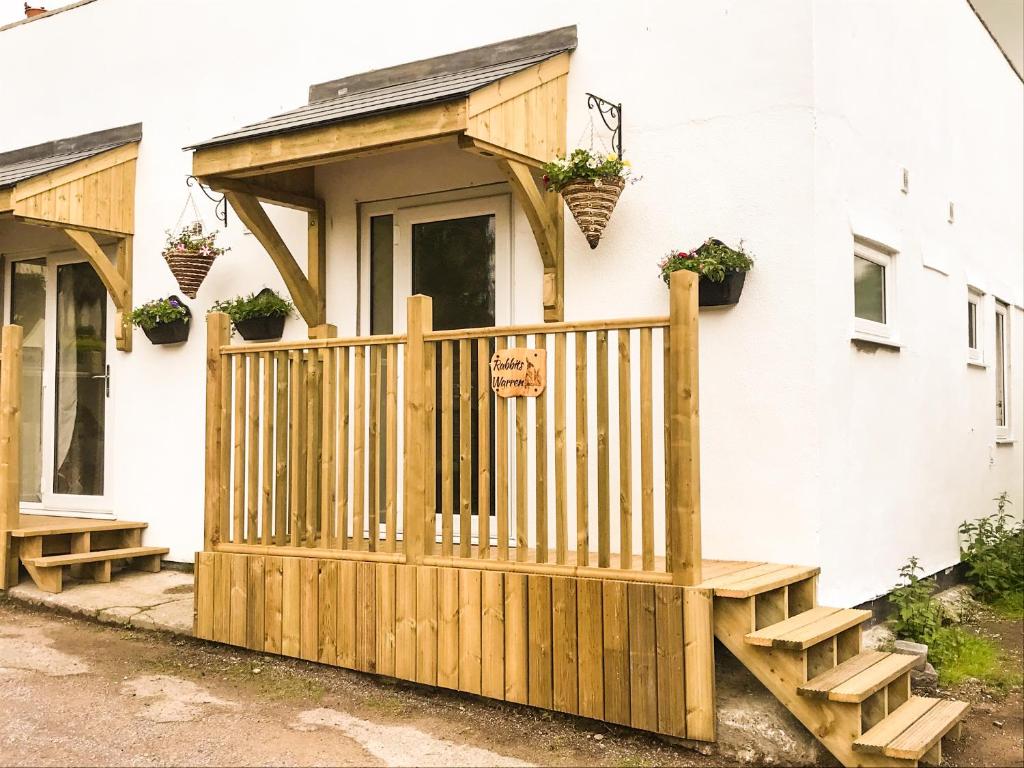 Rabbits Warren, 2 Single Bed Holiday Let in The Forest of Dean في Blakeney: منزل مع شرفة خشبية مع نباتات الفخار