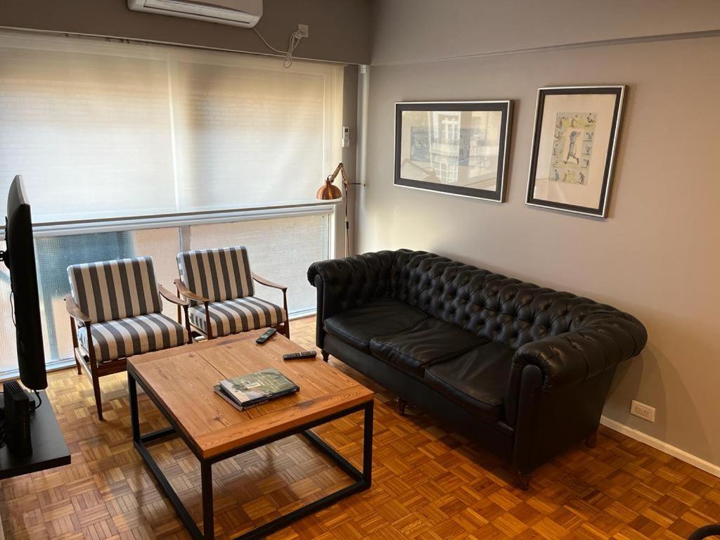 a living room with a black leather couch and two chairs at Castex Palermo Chico in Buenos Aires