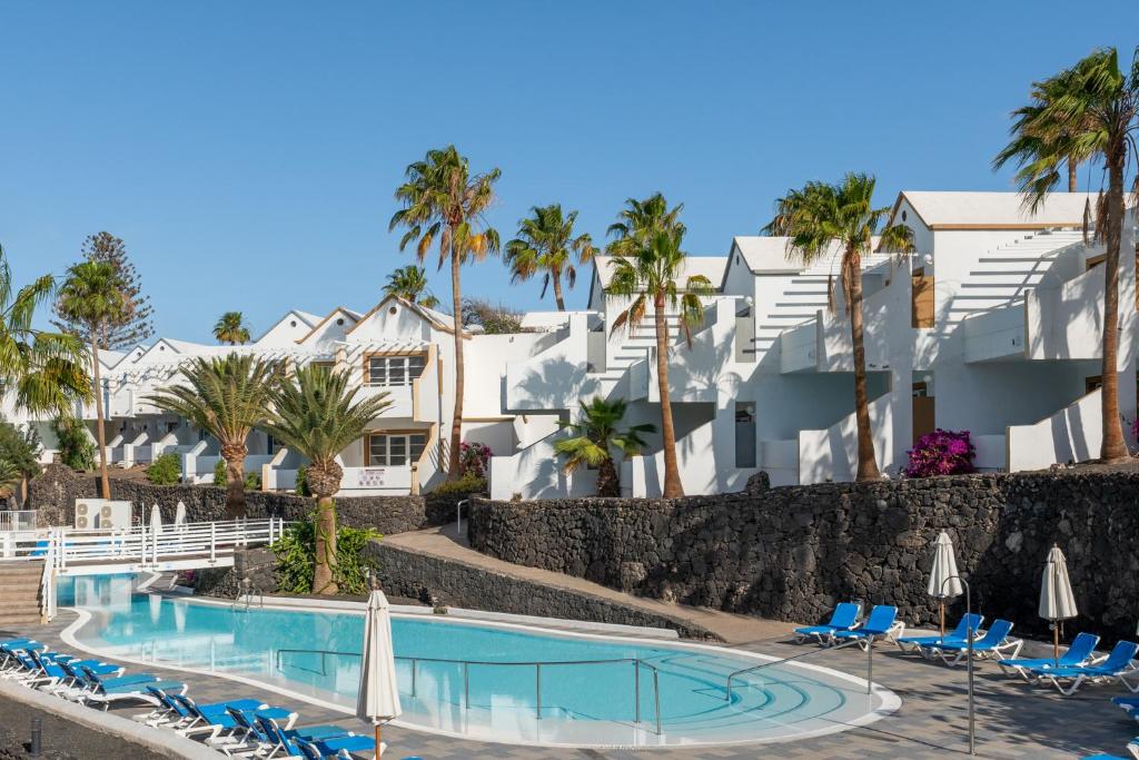 a resort pool with chairs and palm trees at Apartamentos LIVVO Morromar in Puerto del Carmen