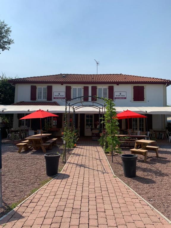 un bâtiment avec des tables de pique-nique et des parasols rouges dans l'établissement Maison de Mézos, à Mézos