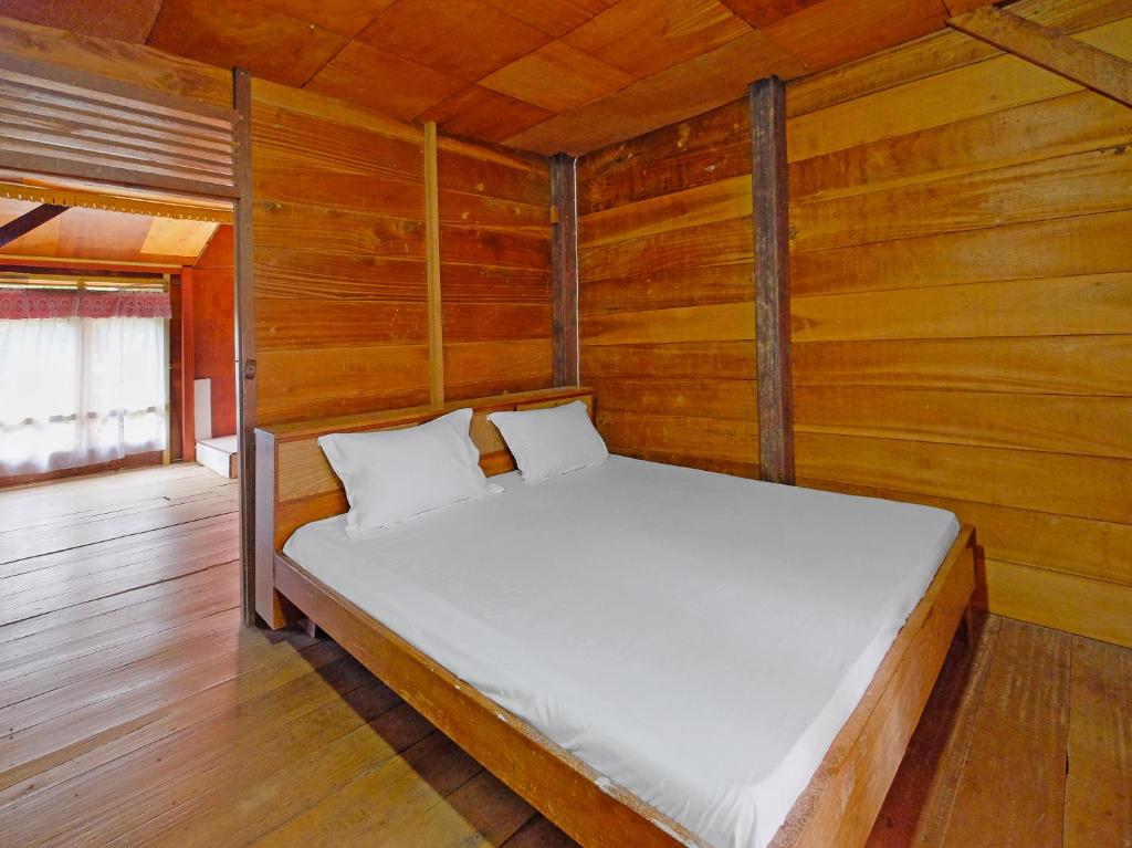 uma cama num quarto com paredes de madeira em OYO Homes 91167 Tatto Bara Homestay em Madandan