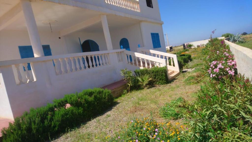 a white house with a white fence and some flowers at Villa en el campo sobre el mar in Ras El Ma