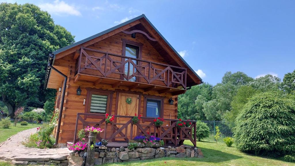 a log cabin with a balcony and flowers in the yard at Domki pod Lipą. in Liszna