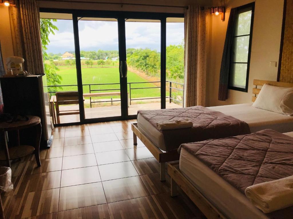 a room with two beds and a balcony with a view at บ้านกลางเกาะ รีสอร์ท in Uthai Thani