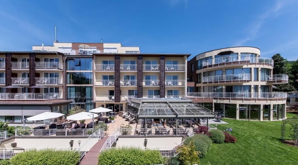 a large building with tables and umbrellas in front of it at das Balance - Spa & Golf Hotel am Wörthersee in Pörtschach am Wörthersee