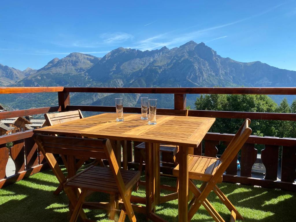- une table en bois avec des verres sur un balcon avec des montagnes dans l'établissement Appartement Montagne Puy Saint Vincent 1800 - Résidence Dame Blanche 3 étoiles, à Puy-Saint-Vincent